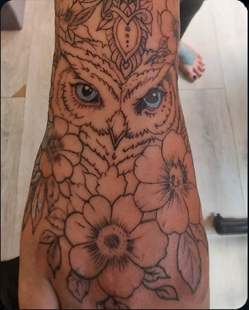 Owl surrounded by flowers and ornamental details tattooed on the forearm