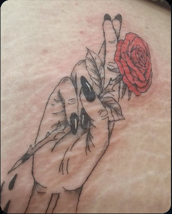Two hands holding a red rose tattoo with black and grey shading and colour detail